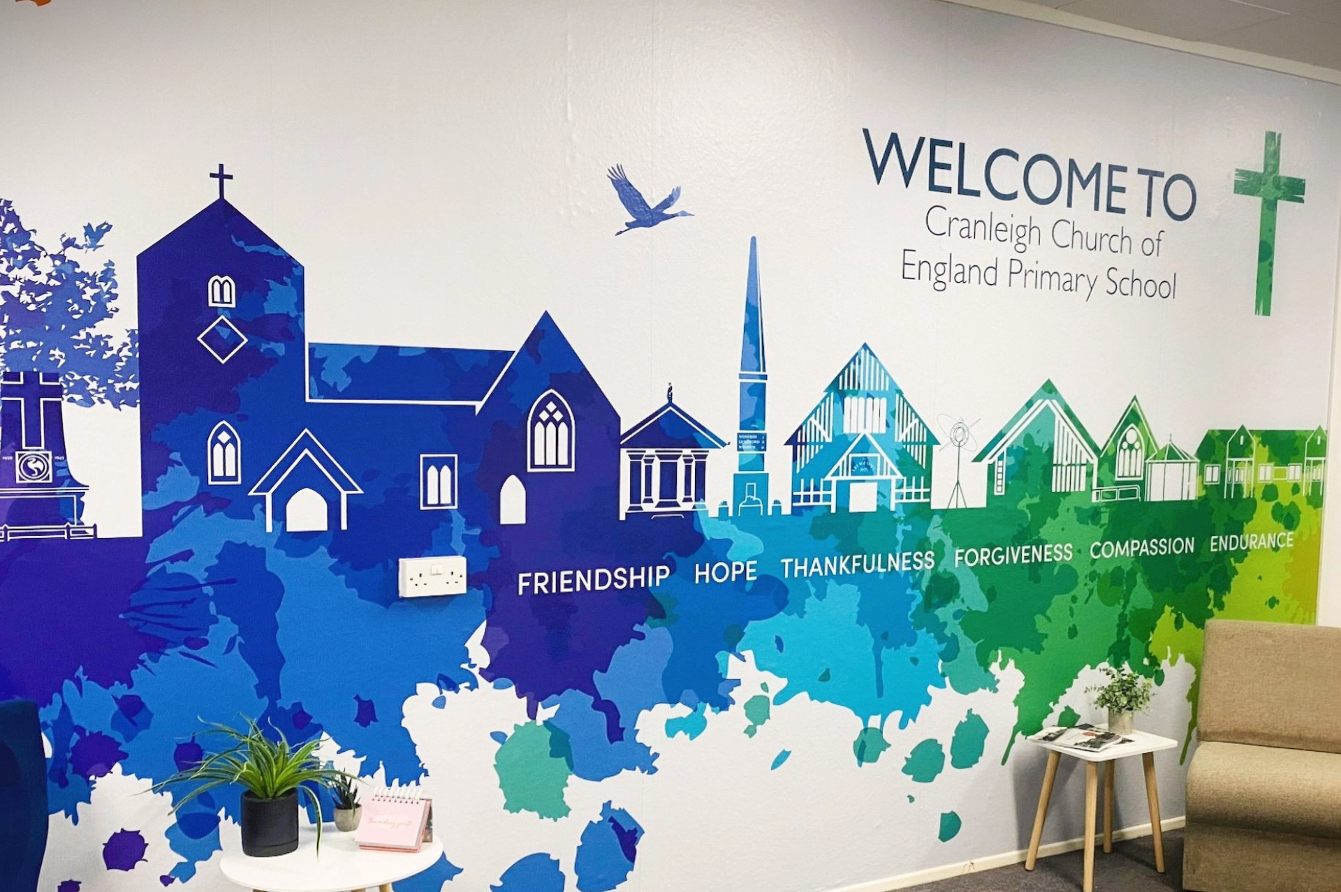 Photo of a wall in Cranleigh Church of England Primary School decorated with images of buildings from the village and the values of the school: friendship, hope, thankfulness, forgiveness, compassion and endurance