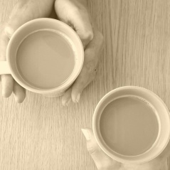 Hands holding two mugs of tea at a table