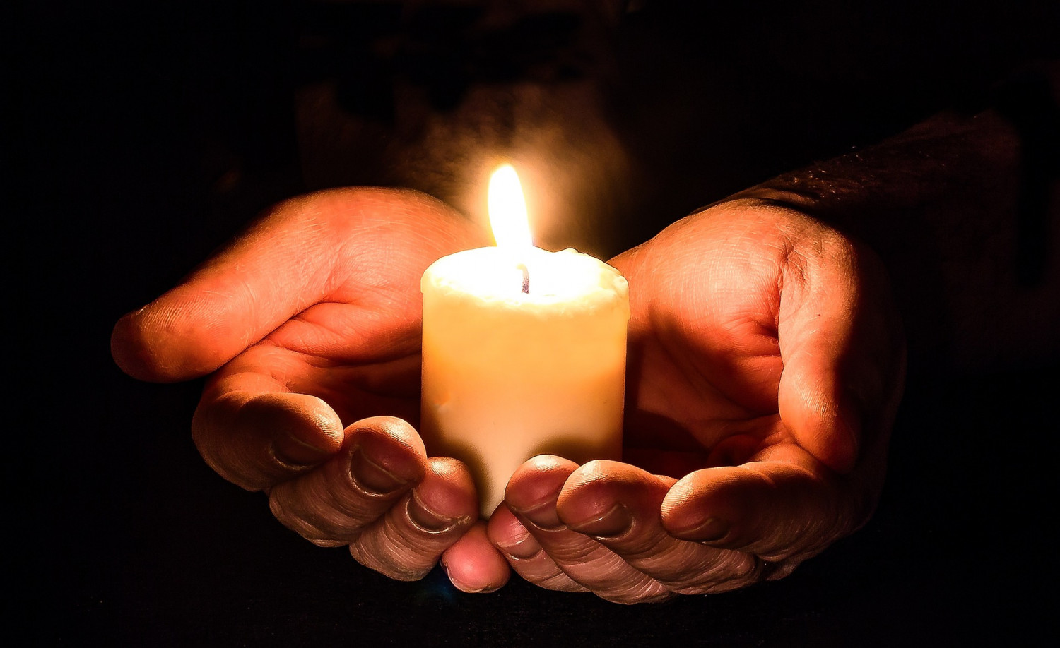 Hands holding a burning candle in the dark