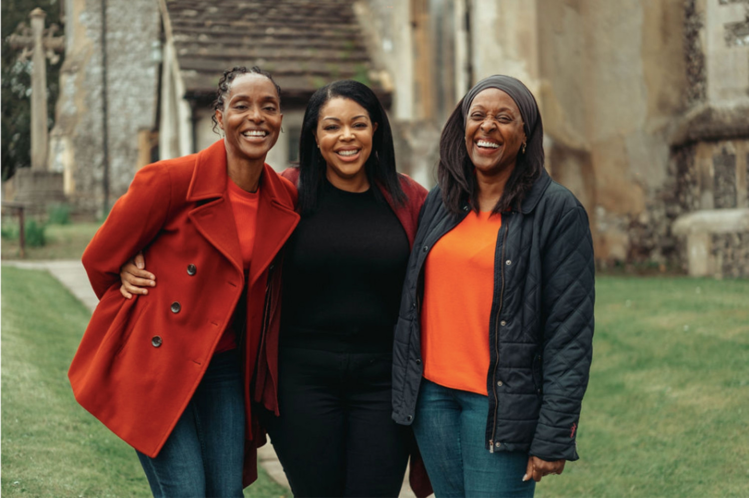 Three women stood in a churchyard smiling at the camera with arms around one another.