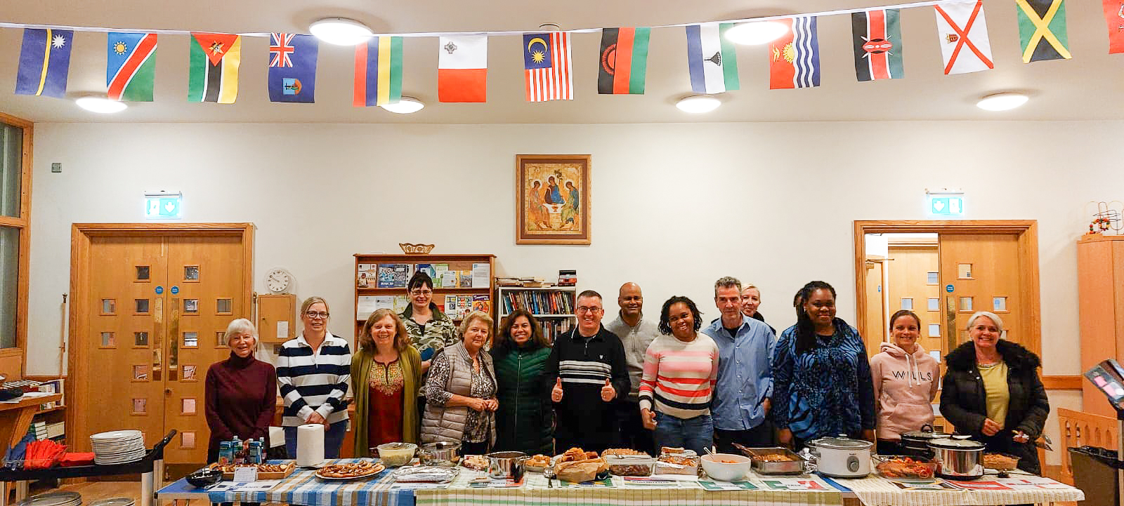 People of various nationalities stood behind a table of cooked food and under bunting made up of international flags