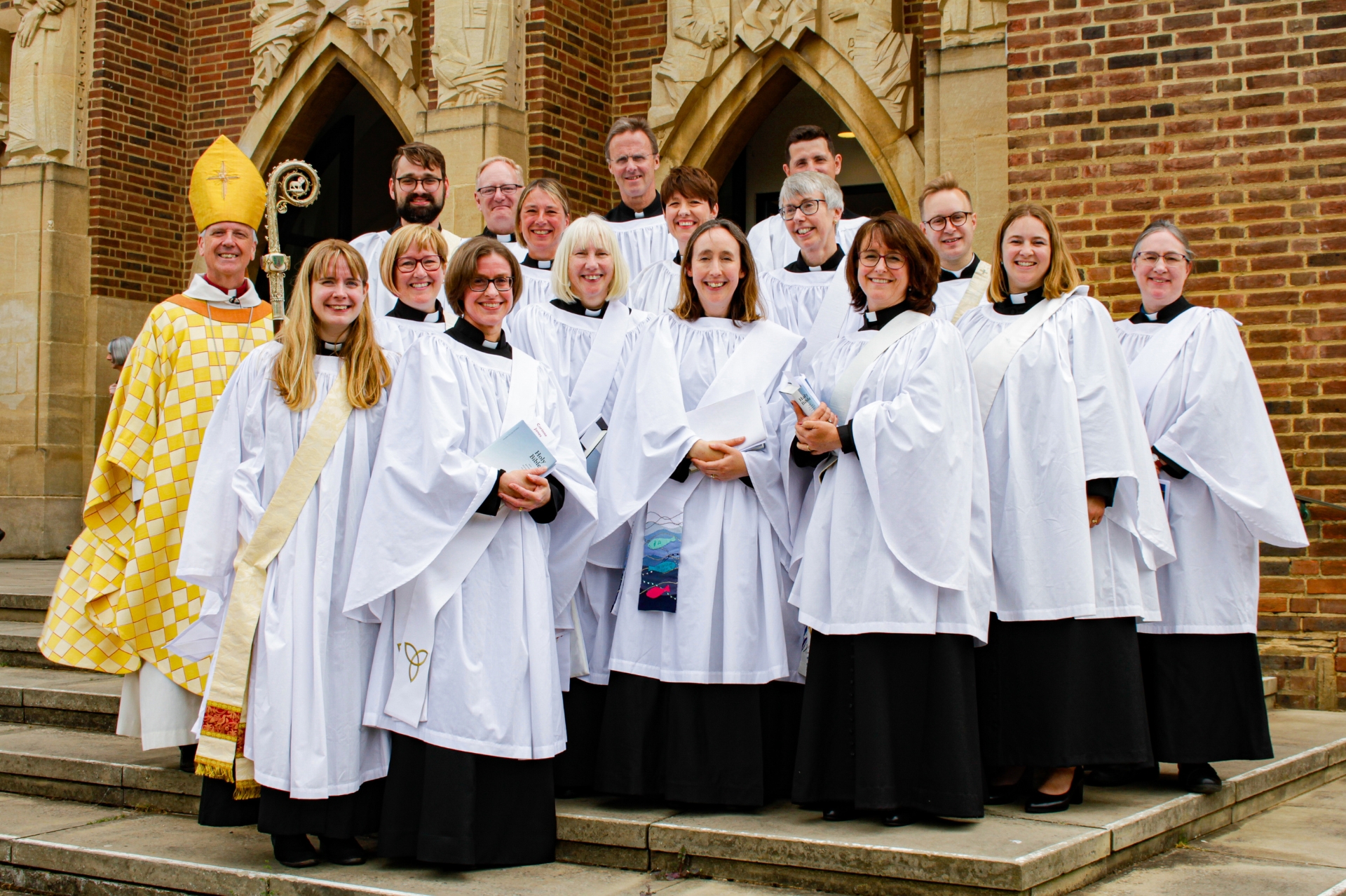 16 new deacons on the steps of Guildford Cathedral celebrating their ordination with the Bishoop of Guildford