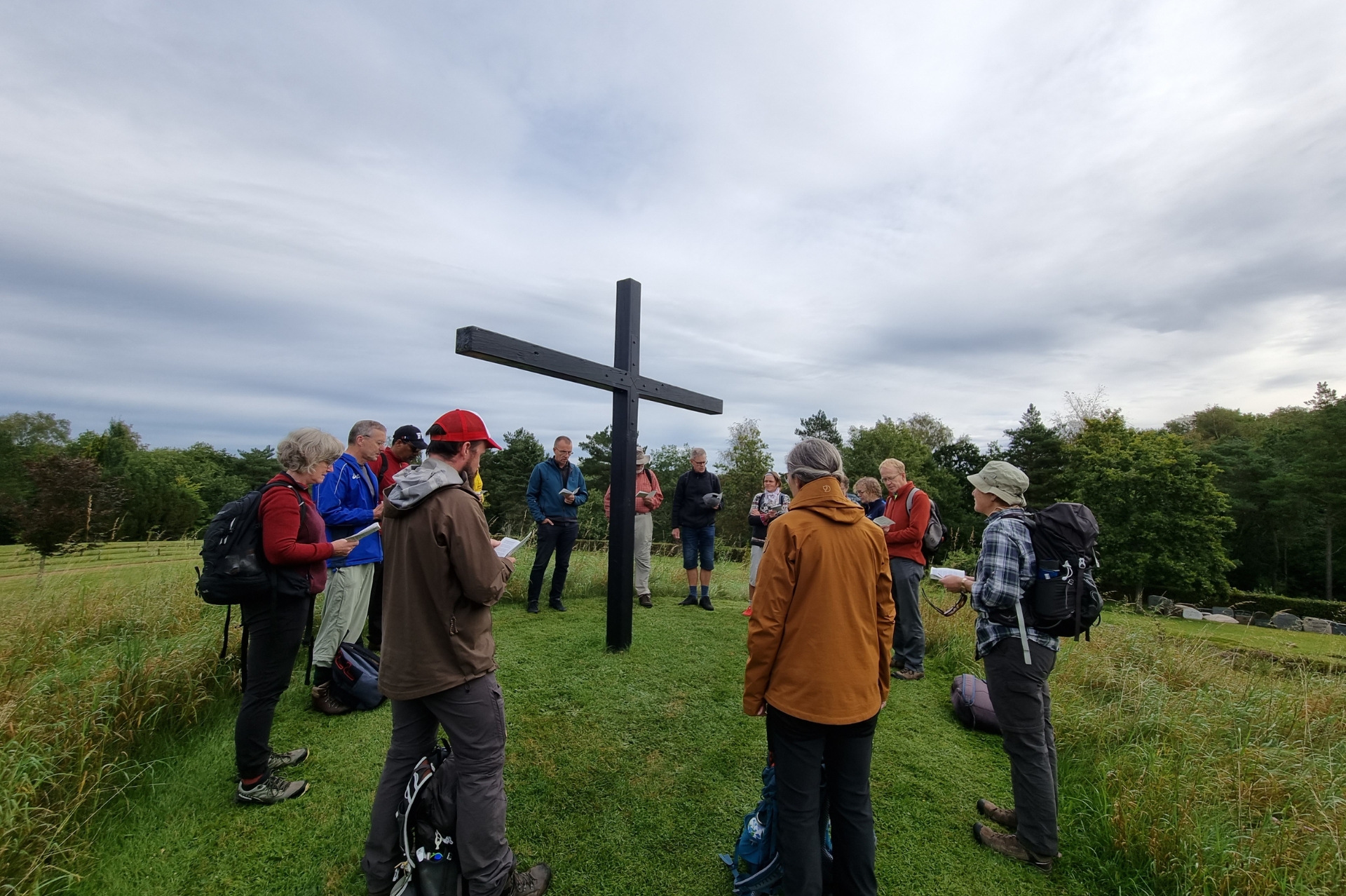 Group of people outside gathered around a wood cross holding hymn sheets