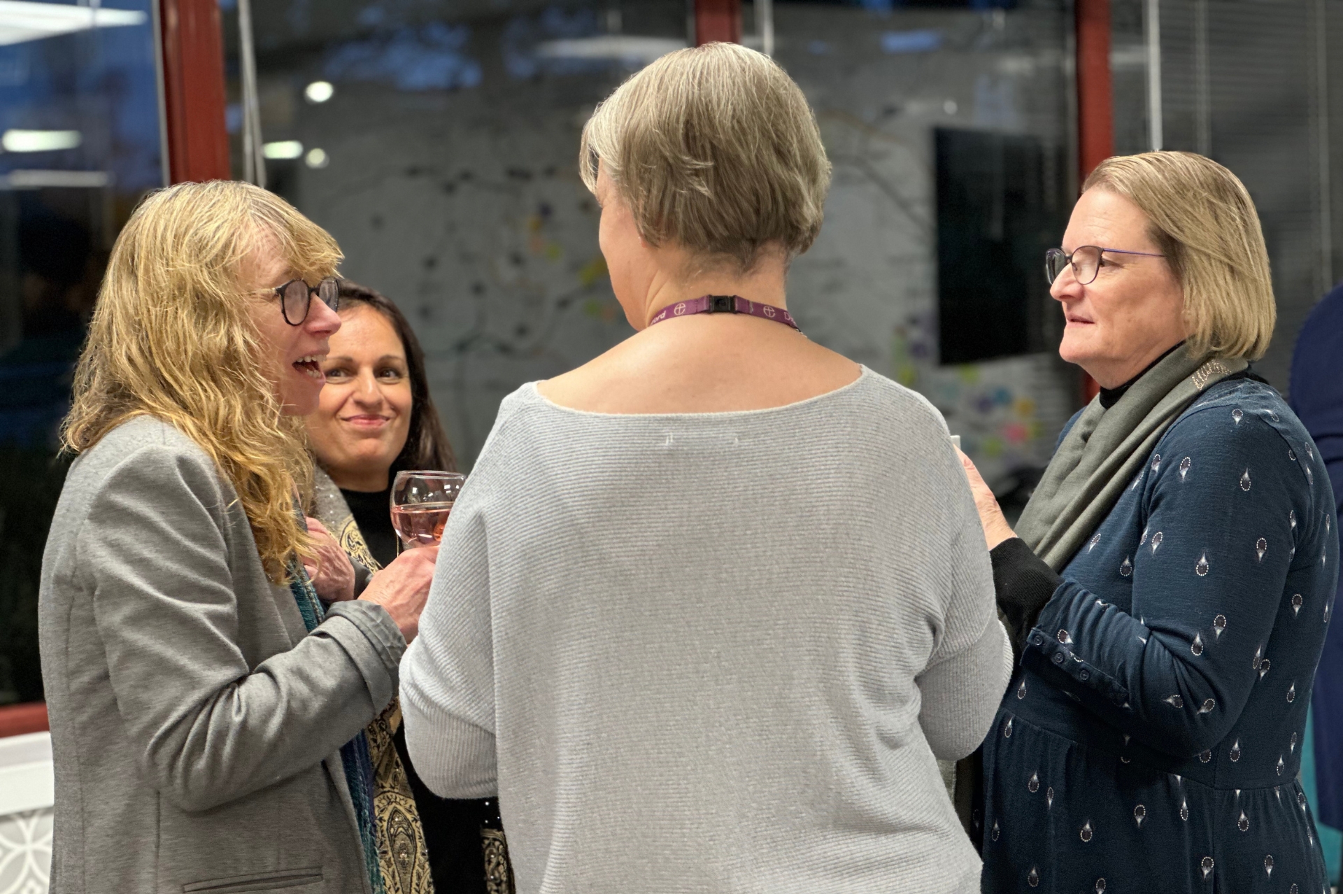 A groups of four women stood together in a room in conversation with one another