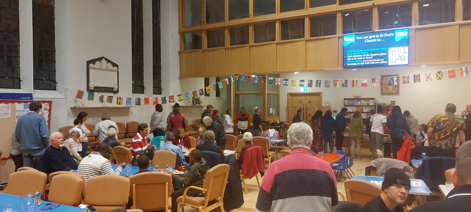 People in a large room sat at tables and queuing for food