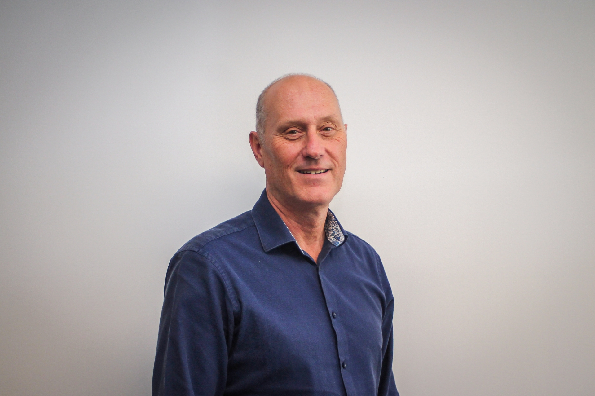 Paul Francis wearing a navy blue shirt staninding in front of a grey wall