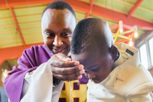 Boy getting baptised by a vicar wearing a purple robe