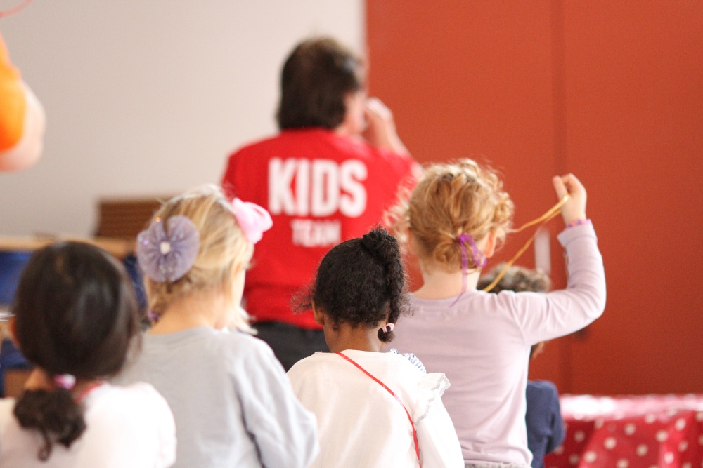 Young children attending a kids group, led by an adult wearing a red Kids Team t-shirt