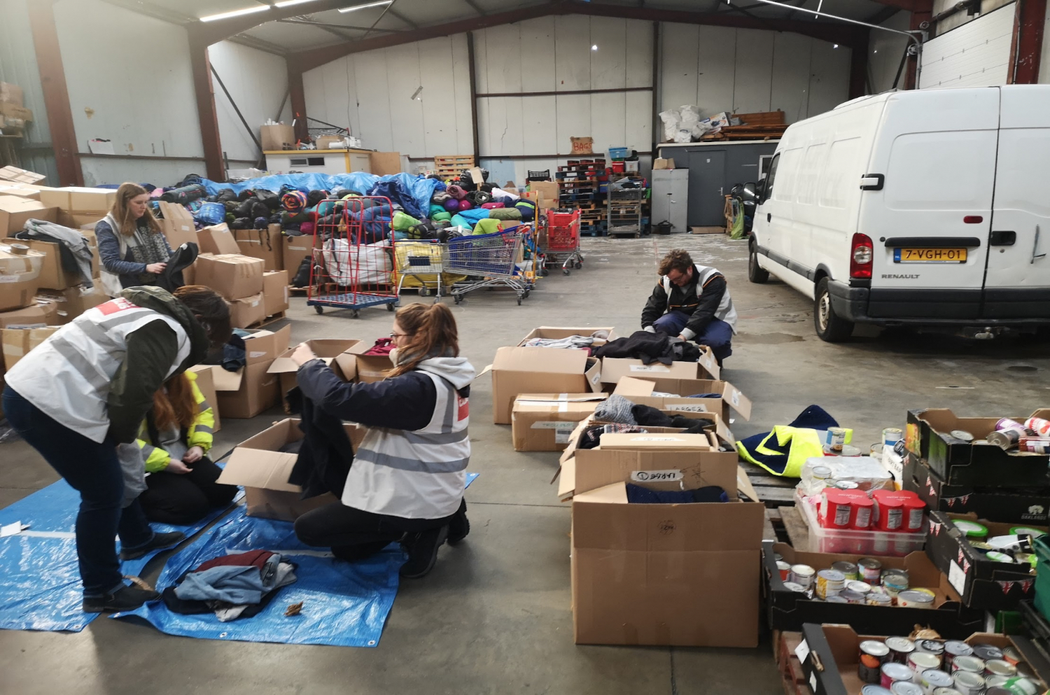 Workers in hi-vis jackets and a white van in a warehouse sorting through boxes of clothing and food goods
