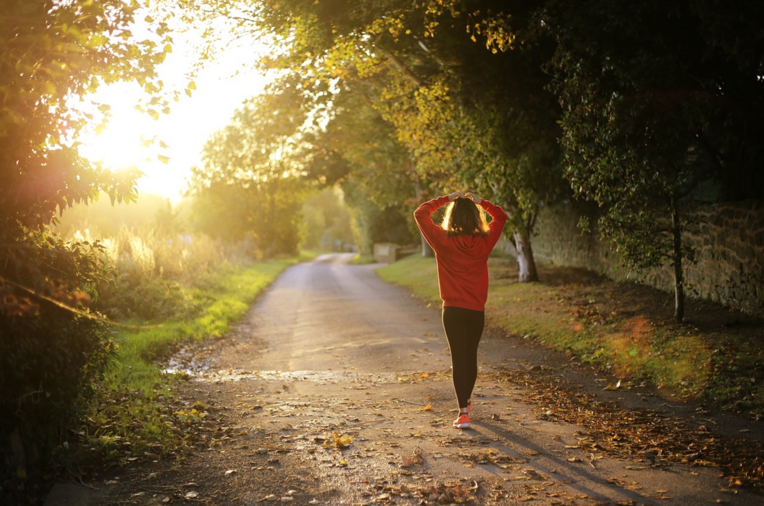 Woman with her hands on her head on an empty countryside road, illuminated by a golden sunset