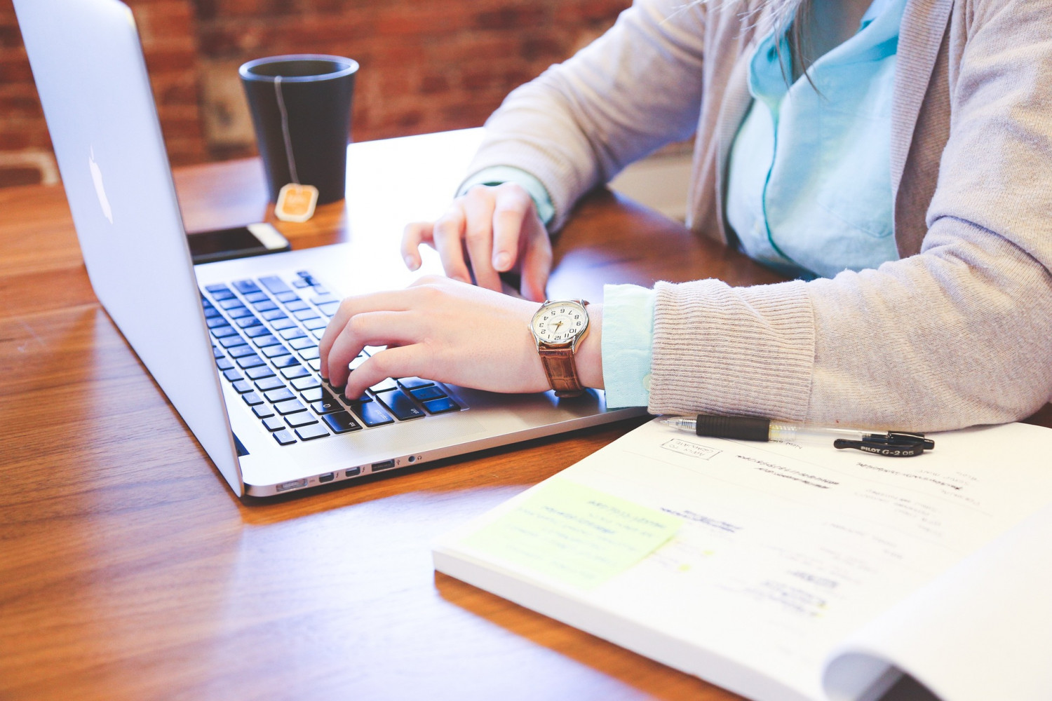 Woman at a desk typing on a Macbook with a cup of tea beside her