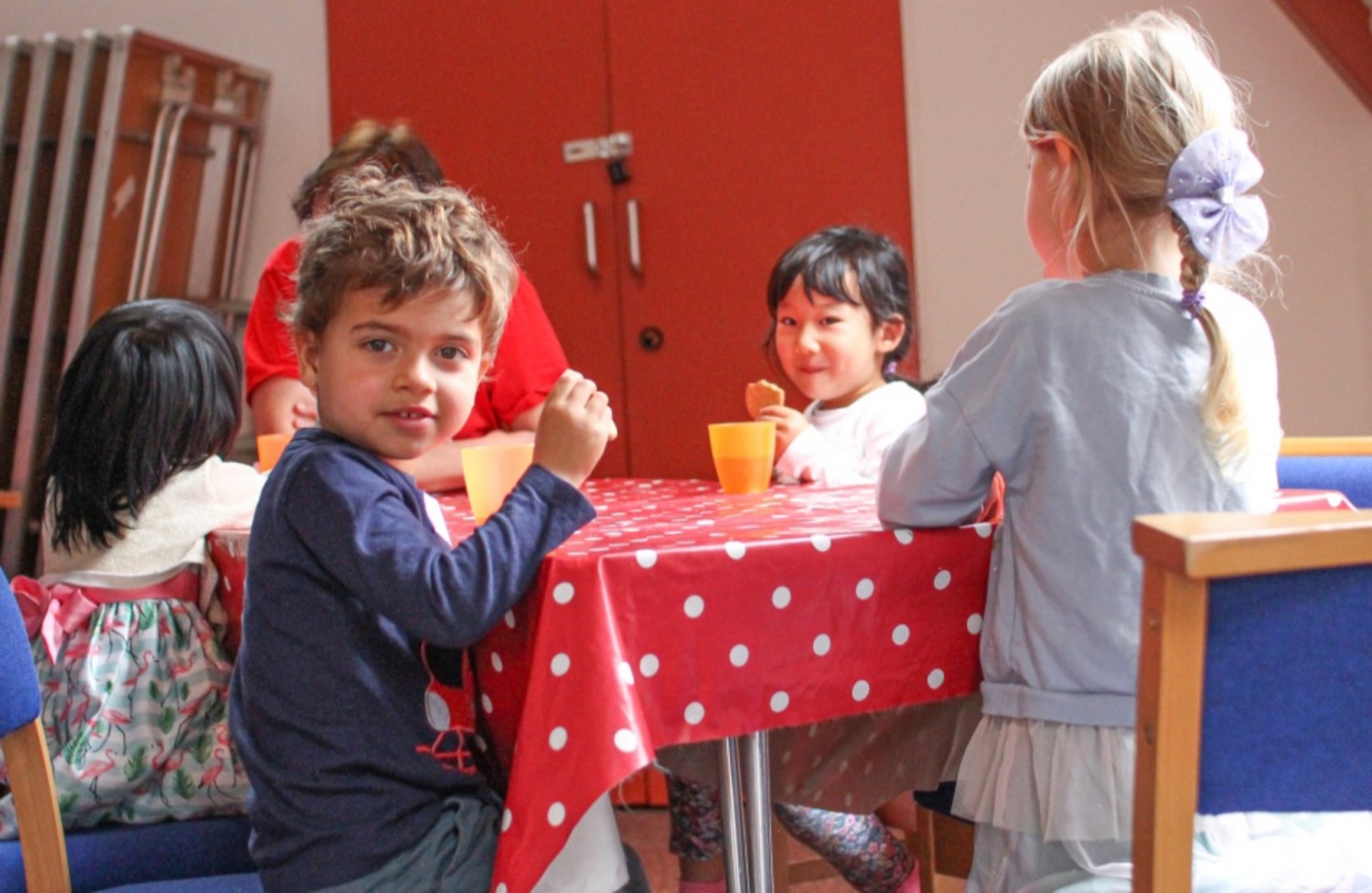 A group of children sat around a table eating biscuits and drinking squash