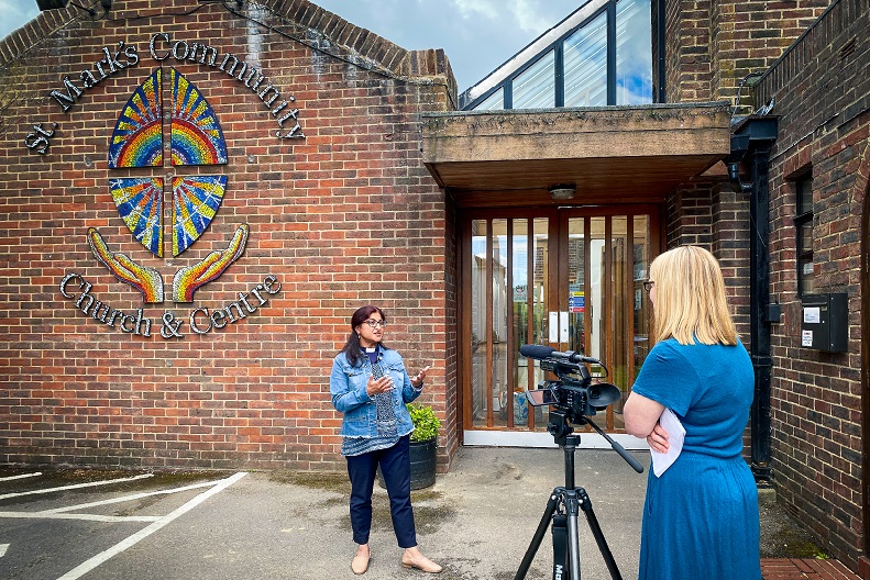 Woman talking to camera with woman with notepad behind camera