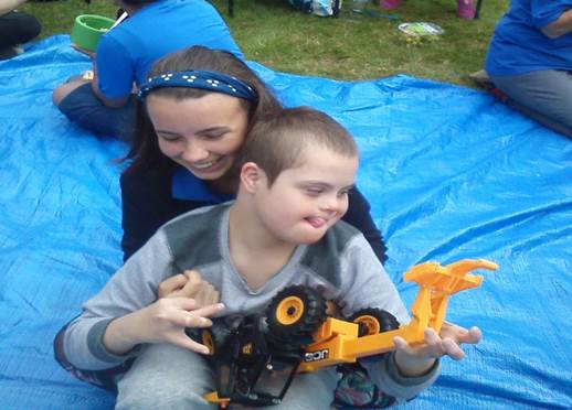 Teenage girl holding up boy with additional needs playing with digger