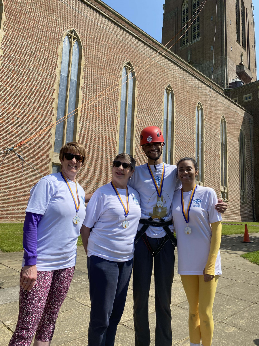 Group four people (three women and a man) wearing matching Guildford Cathedral t-shirts and medals having completed the abseil