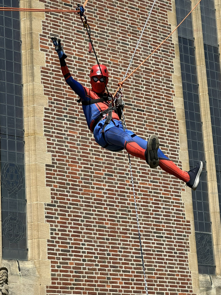 Man wearing spider-man costume waving whilst abseiling down Guildford Cathedral's tower