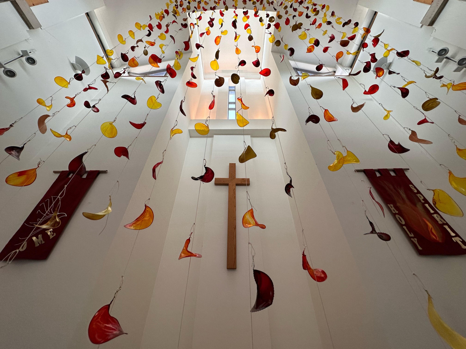 Art installation of resin flame shapes hanging from ceiling of mordern church building with wooden cross in the background