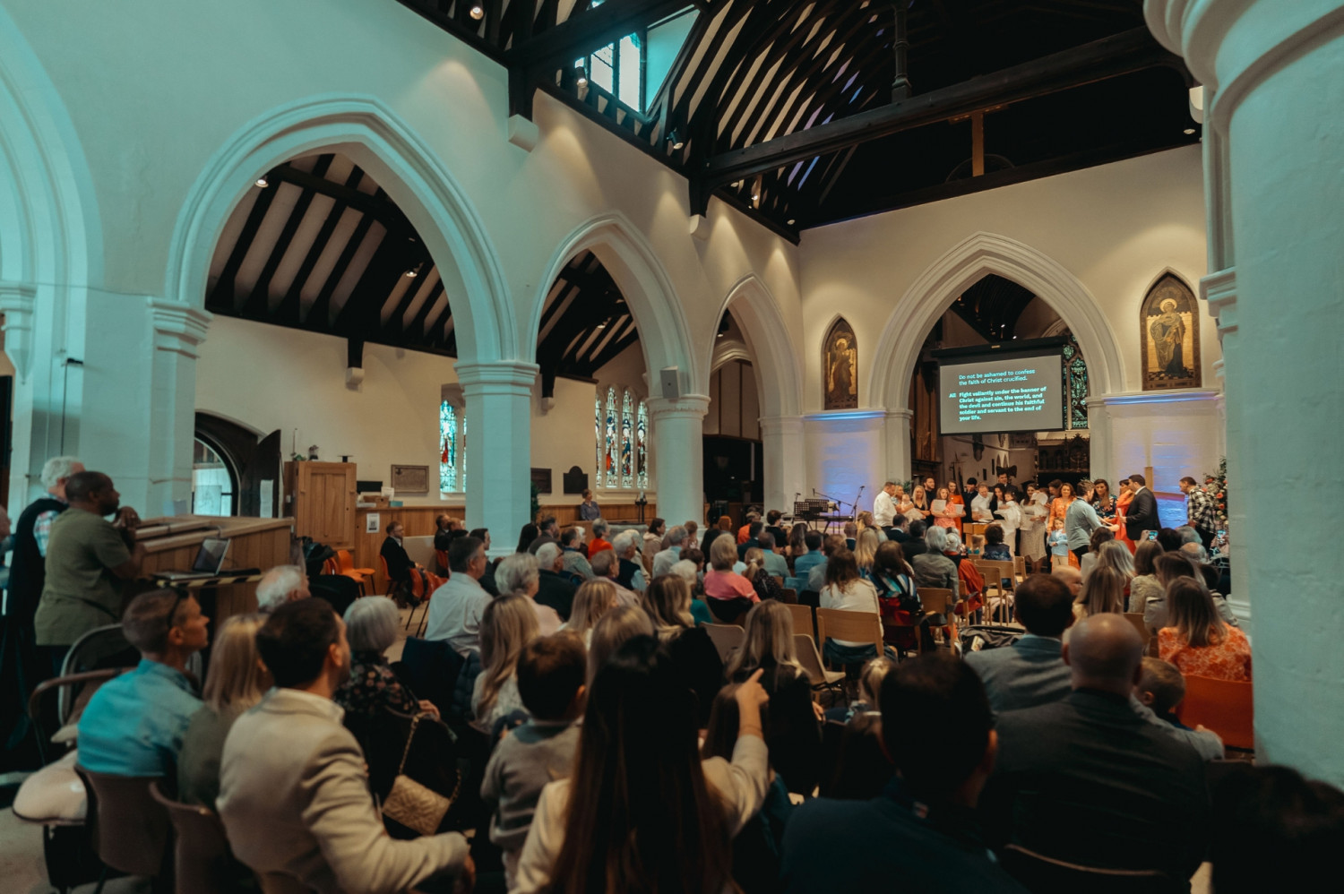 Large church congregation sat in a traditional looking church building with a baptism taking place at the front of the church