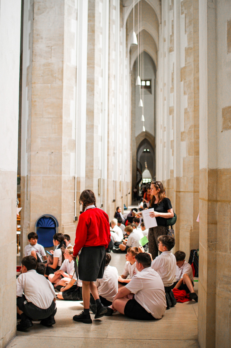 School children stood and sat in a corridor in a cathedral engaging with an activity