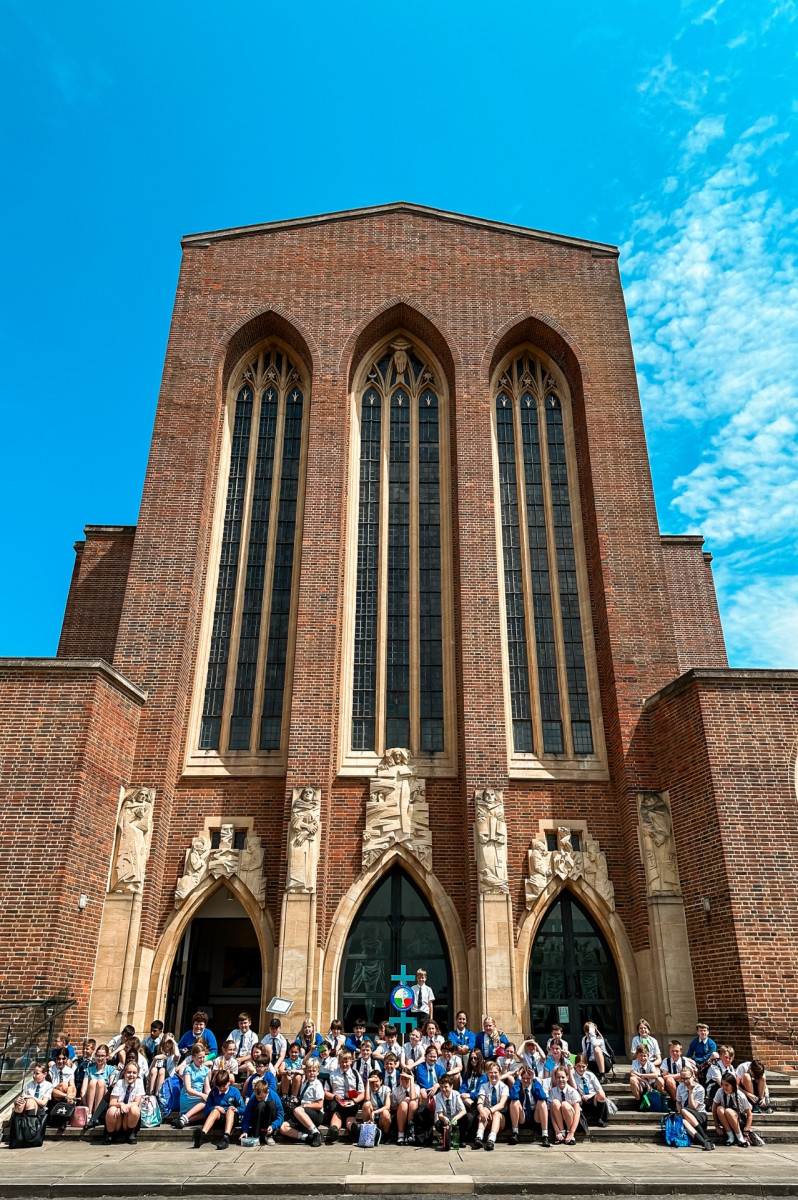 School children sat on the steps of Guildford Cathedral waving their hands in the air on a sunny day