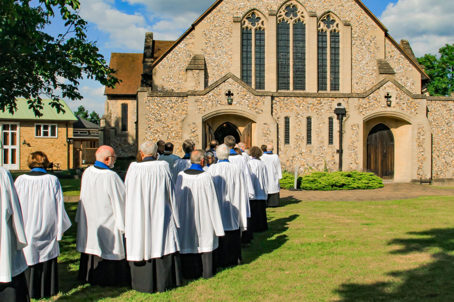Line of robed lay ministers outside a church on a sunny day